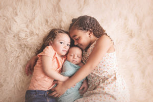 Sisters lovingly holding their newborn brother during their photography session