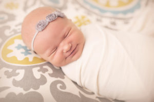 Baby girl smiling while wrapped up in a jersey stretch wrap laying on a patterned backdrop during her photography session