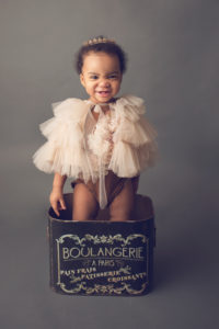 The cutest little one year old standing in a boulangerie bucket wearing a couture tulle cape during her photography session.
