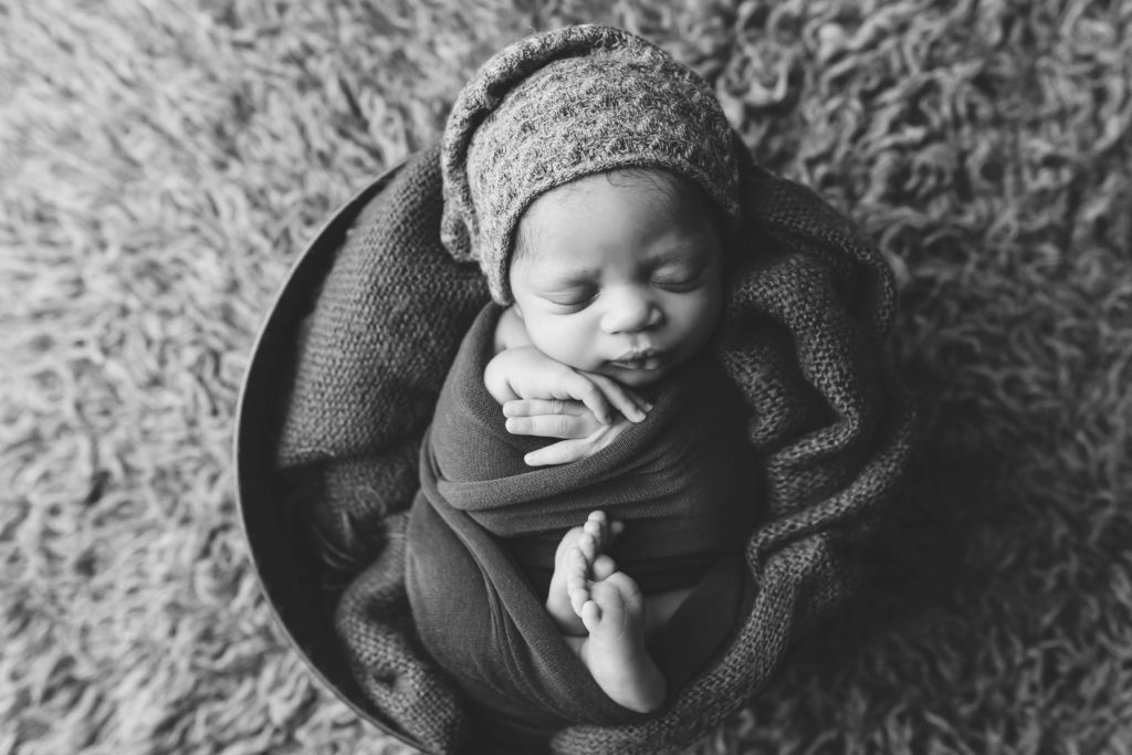 sleeping newborn baby photographed by Joanna Booth photography wrapped in swaddling fabric on a float rug in a cute bonnet 